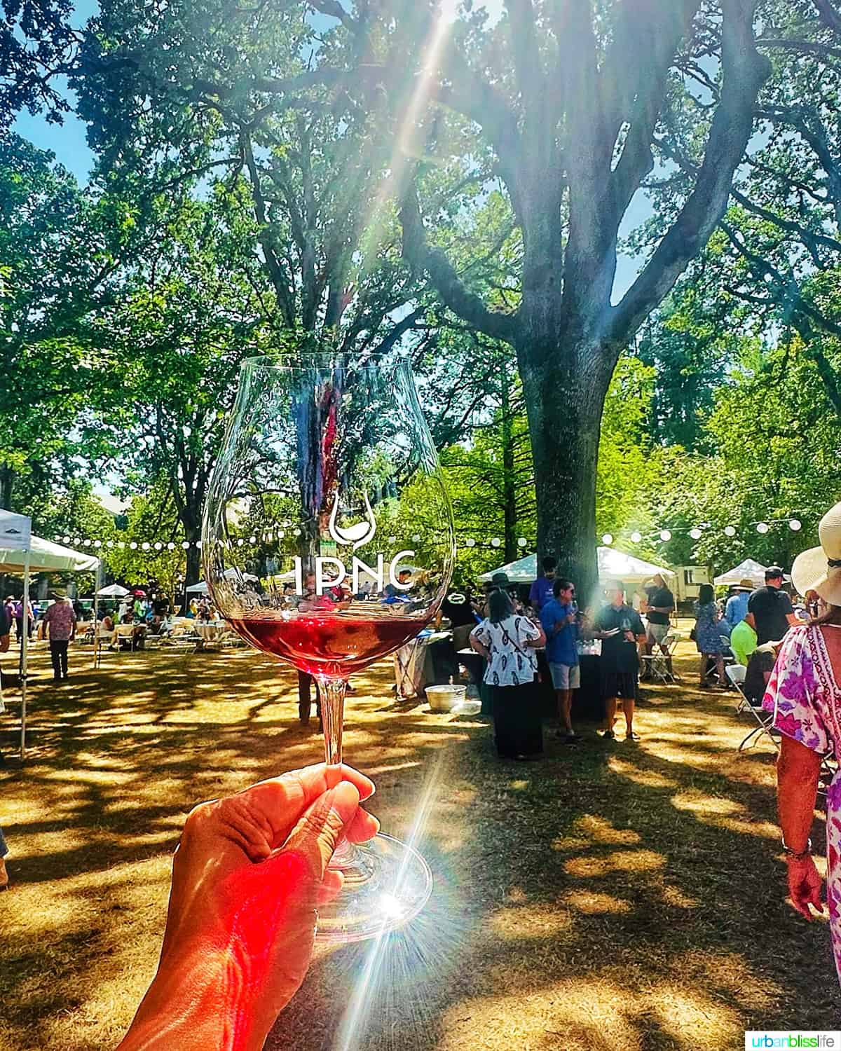 hand holding an IPNC wine glass against an outdoor wine tasting event.