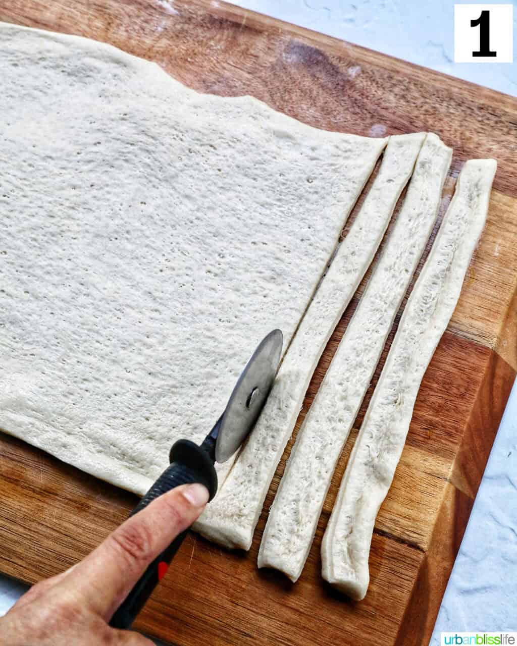 slicing a sheet of pizza dough into thin strips.