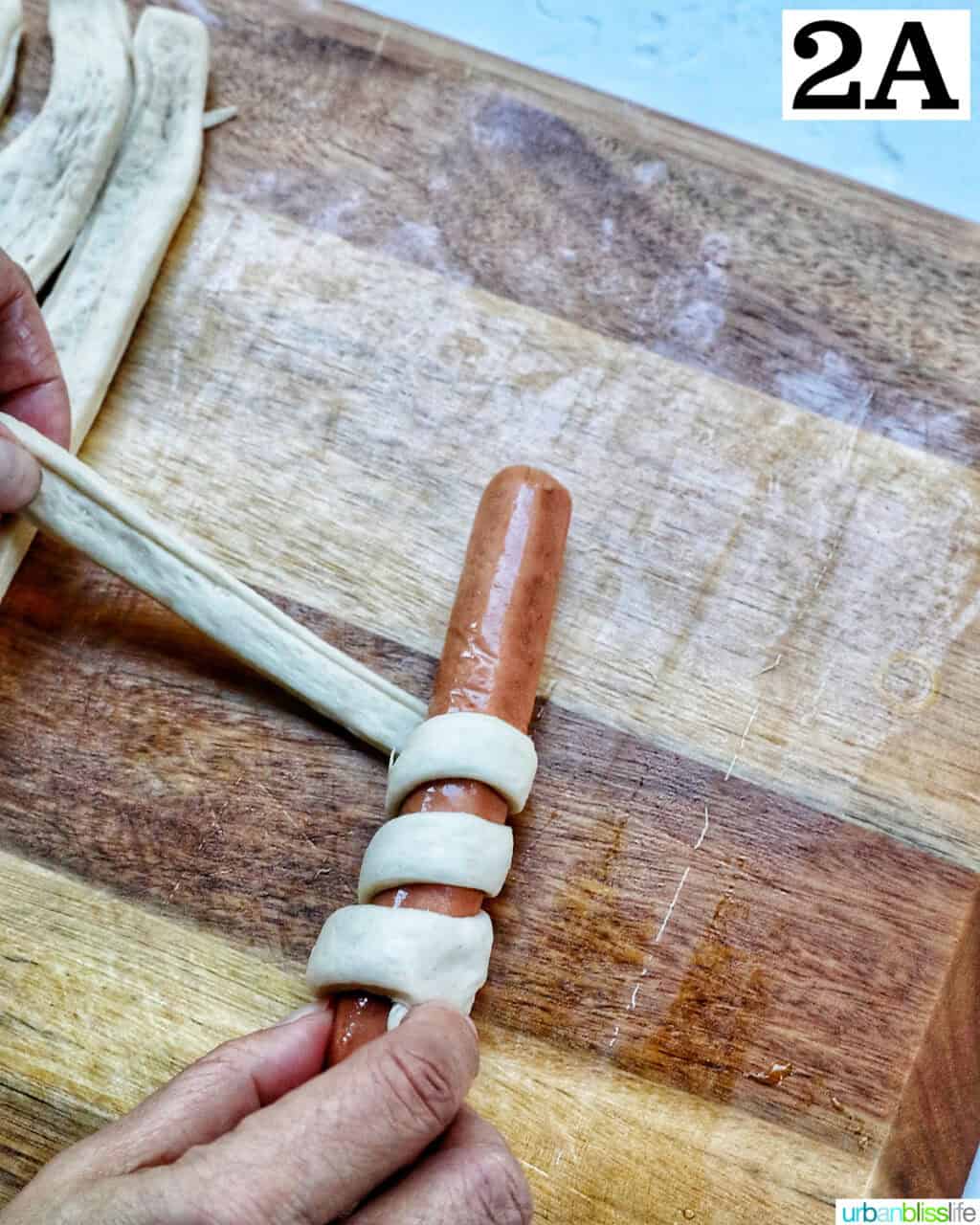 wrapping a strip of pizza dough around a hot dog.