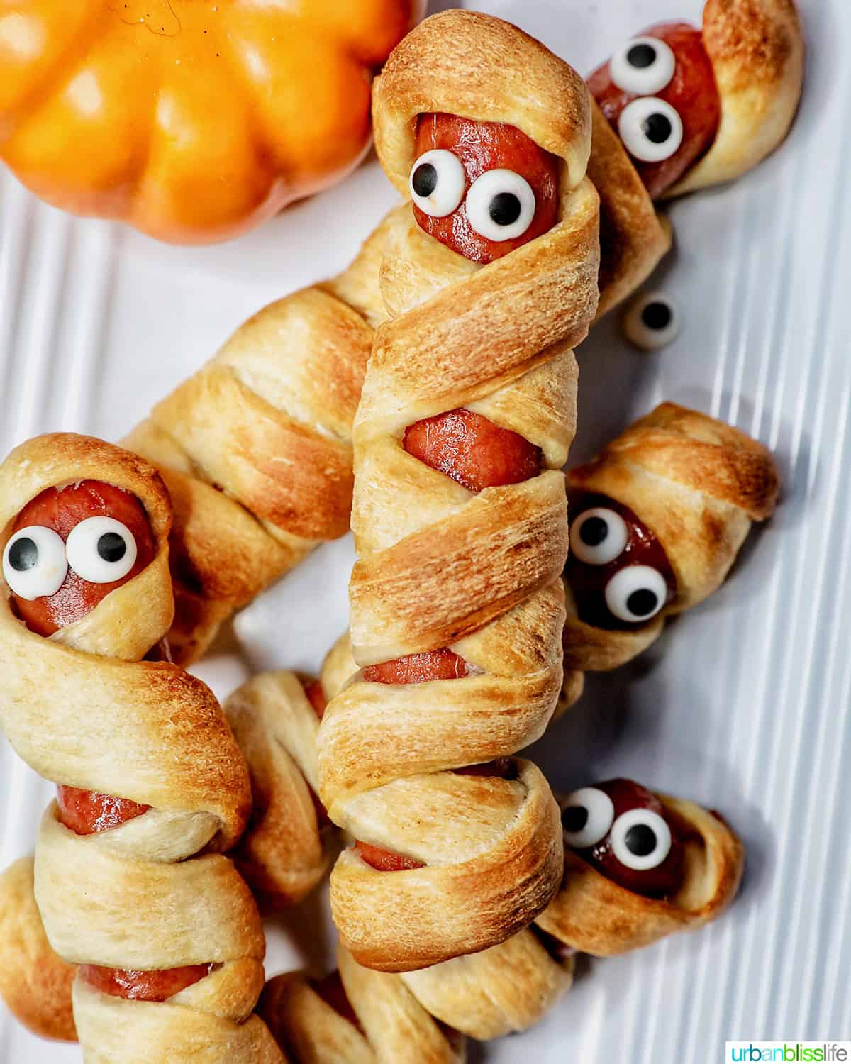 mummy dogs - hot dogs wrapped in pizza dough - stacked on a white plate.