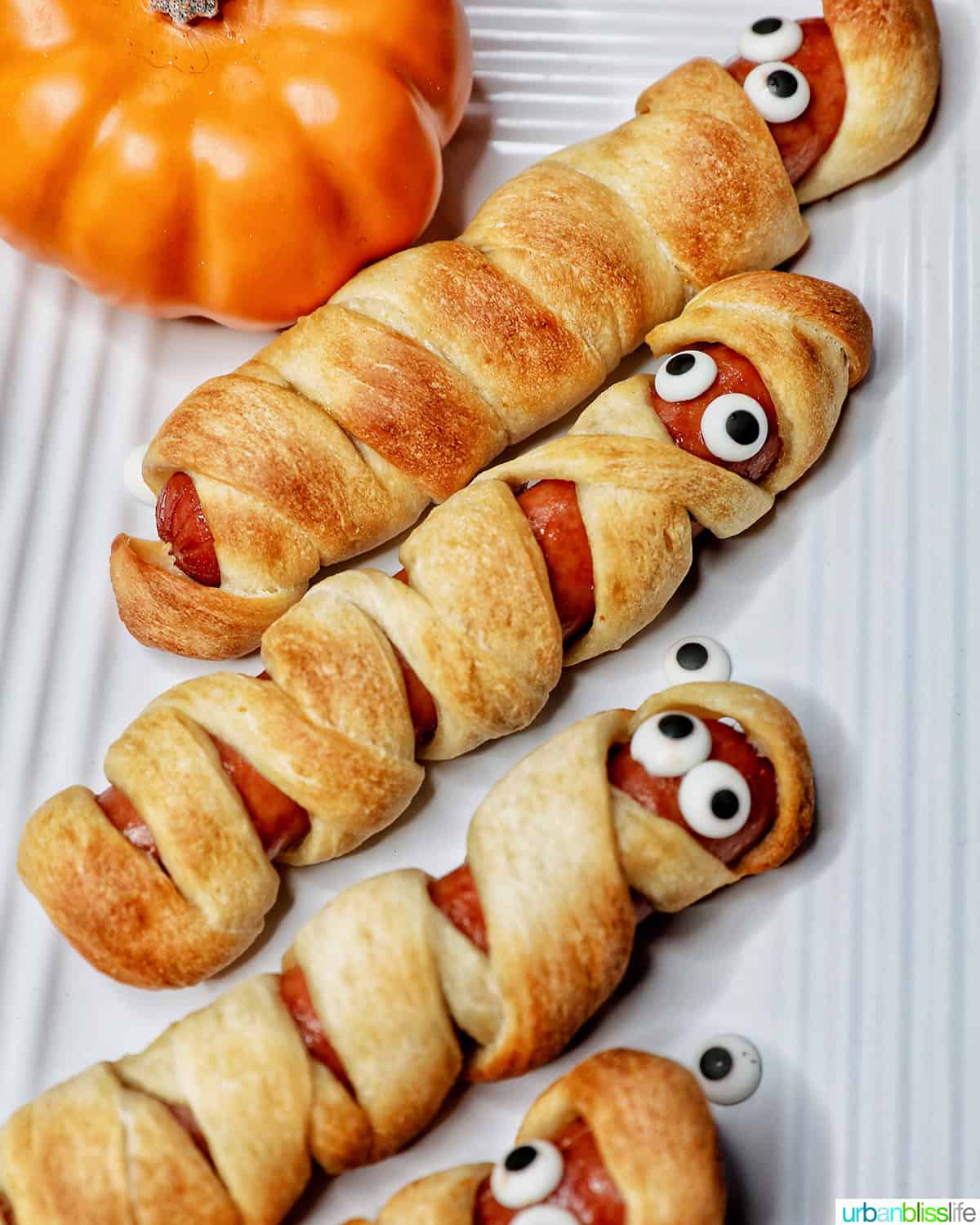 mummy dogs - hot dogs wrapped in pizza dough - stacked on a white plate.