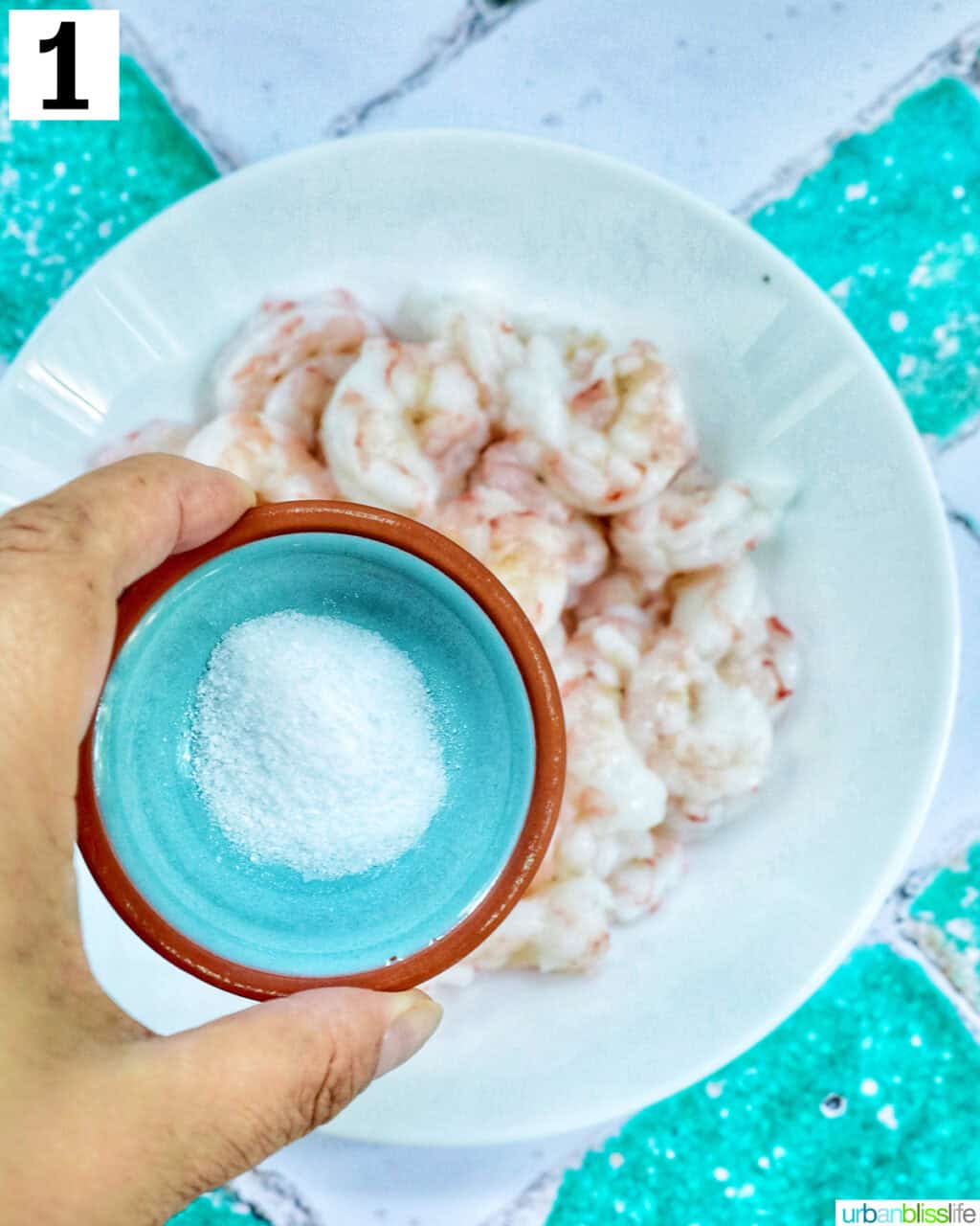 hand holding salt over prawns.