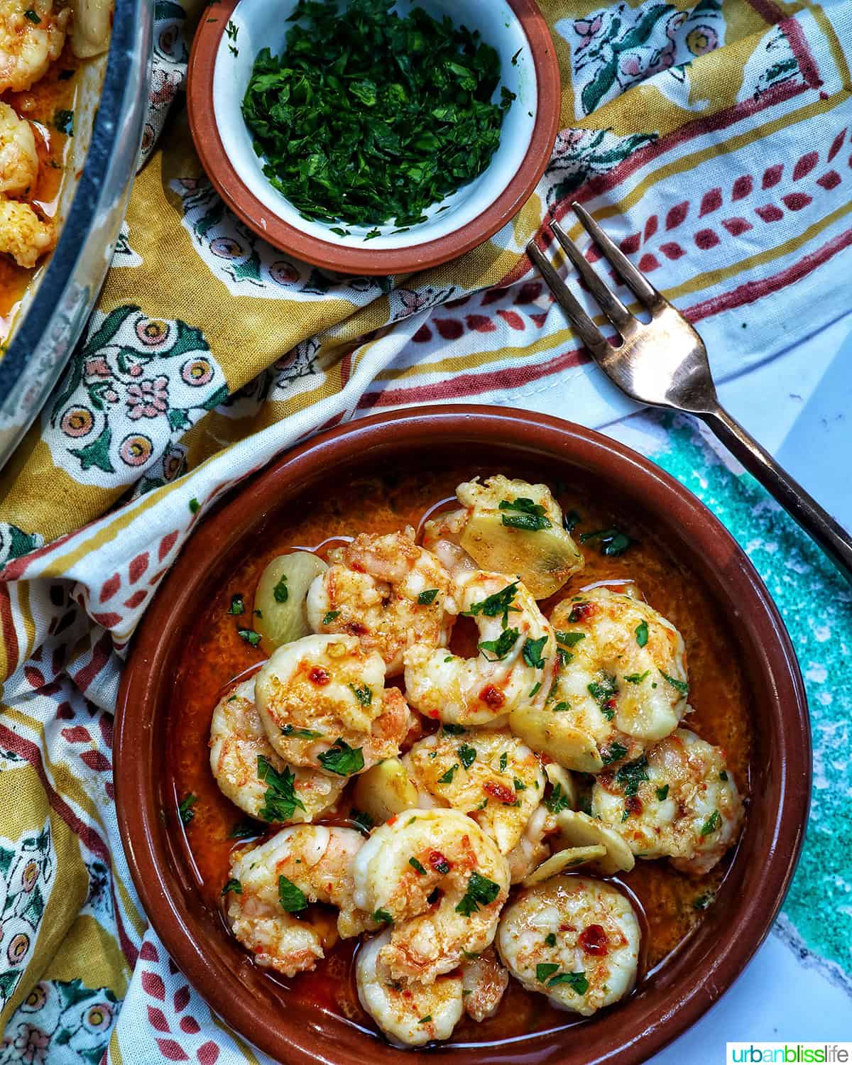 Spanish prawns with garlic and herbs in a traditional Spanish cazuelas, with bowl of parsley and fork.