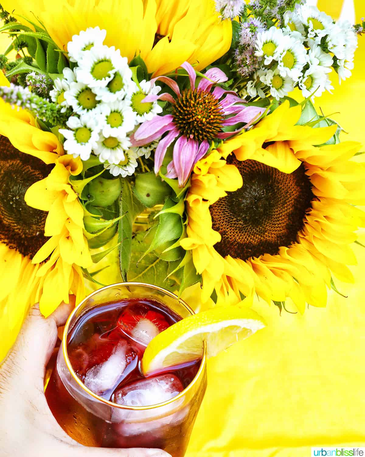 hand holding a glass of glass of tinto de verano wine cocktail with lemon slice by summer flowers.