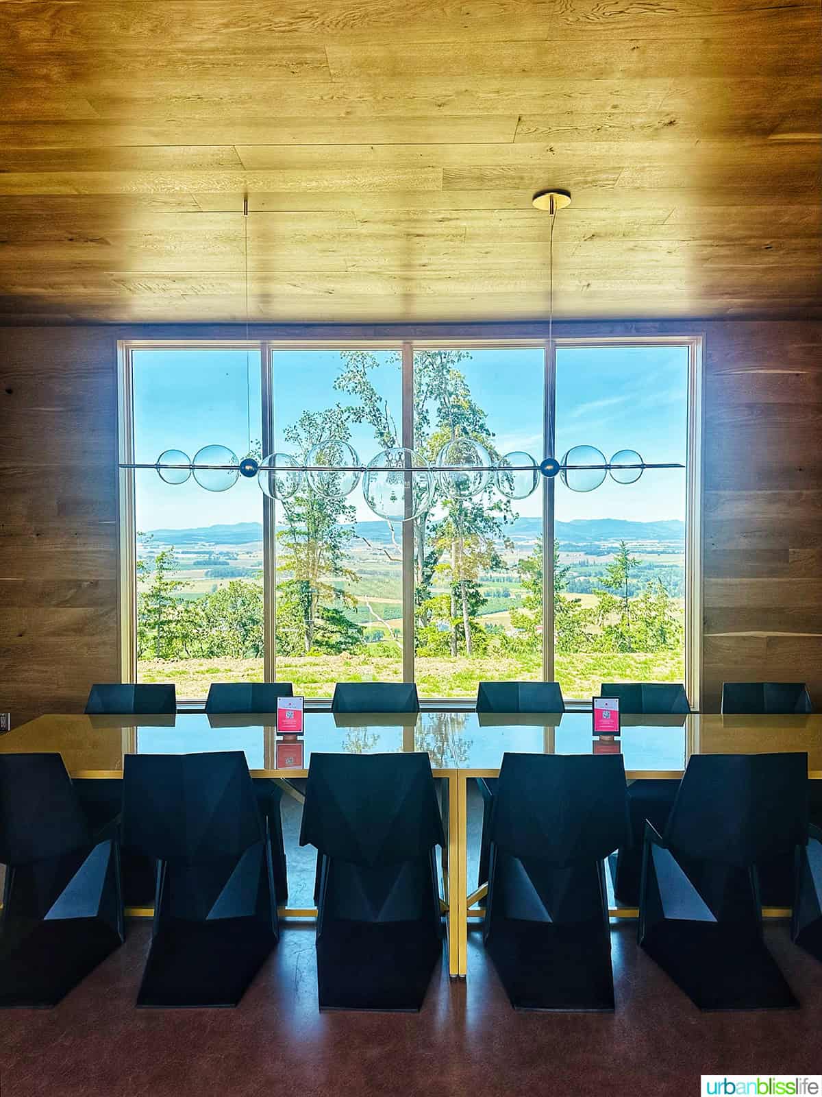 Corollary wines tasting room indoor table and black chairs with picture window looking out at the Willamette Valley.