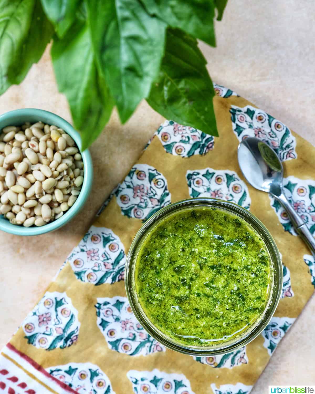 pesto in a mason jar next to a bowl of pine nuts and basil leaves.