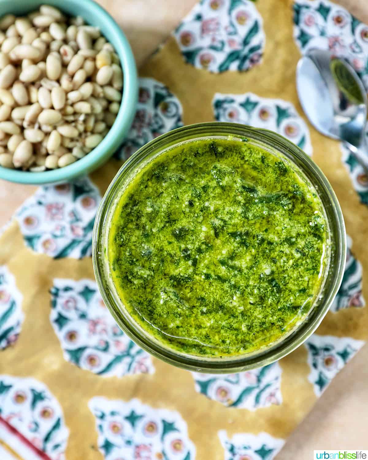 pesto in a mason jar next to a bowl of pine nuts and basil leaves.