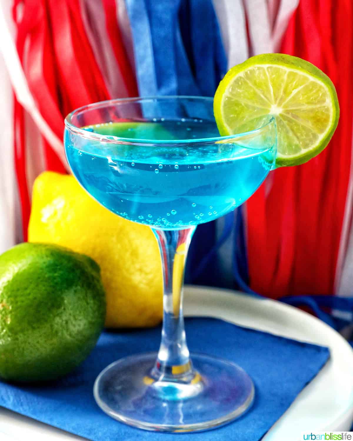 blue wave cocktail with lime slice garnish against red, white, and blue election night decorations.