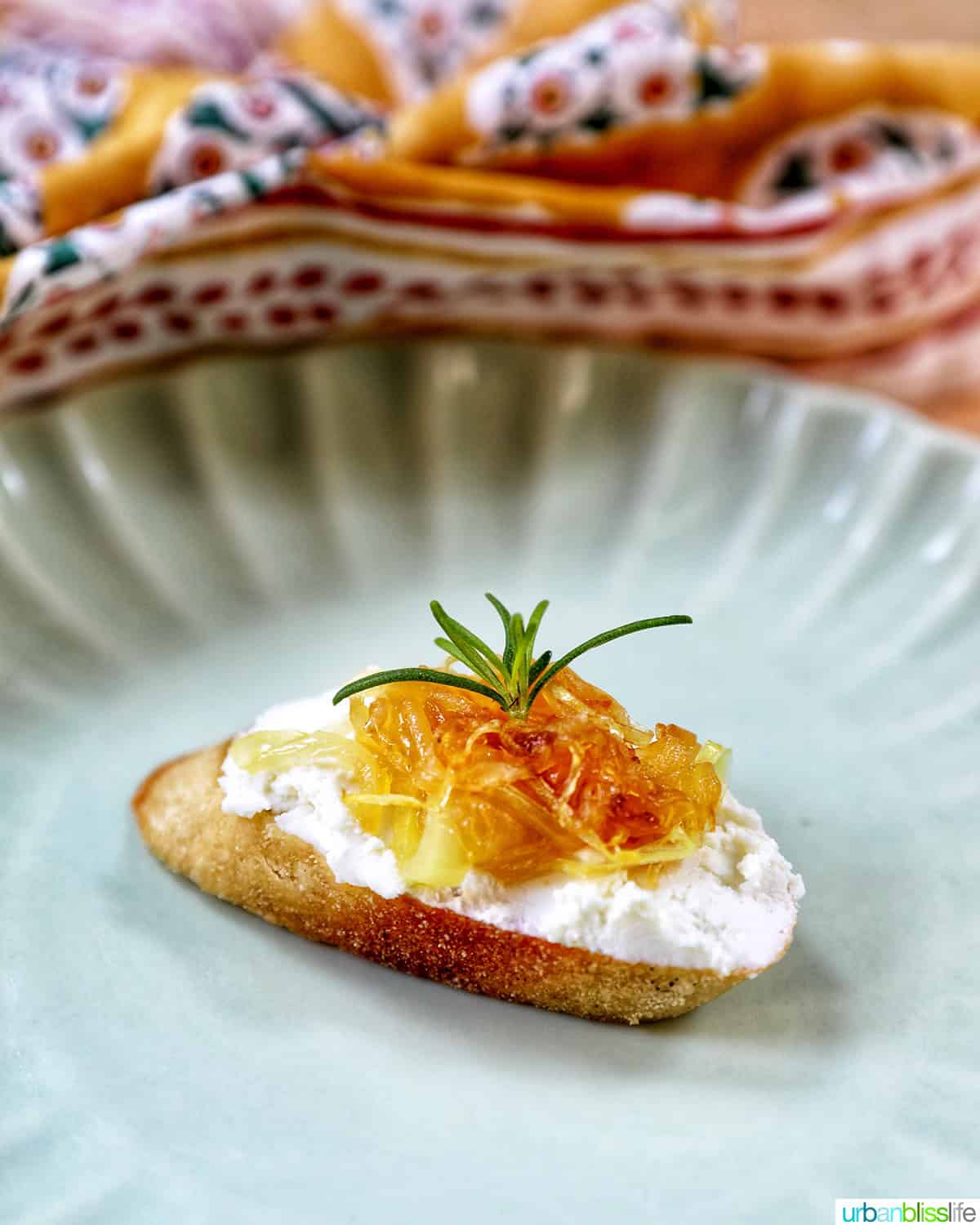 caramelized onions and goat cheese crostini on a plate with rosemary sprig garnish.