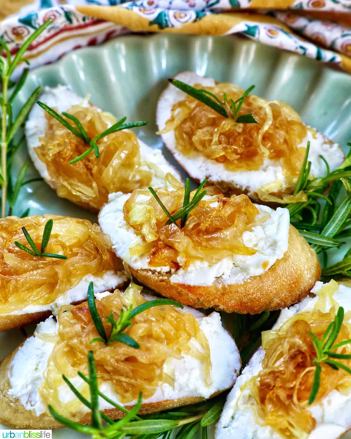 caramelized onions and goat cheese crostini on a plate with rosemary sprig garnish.