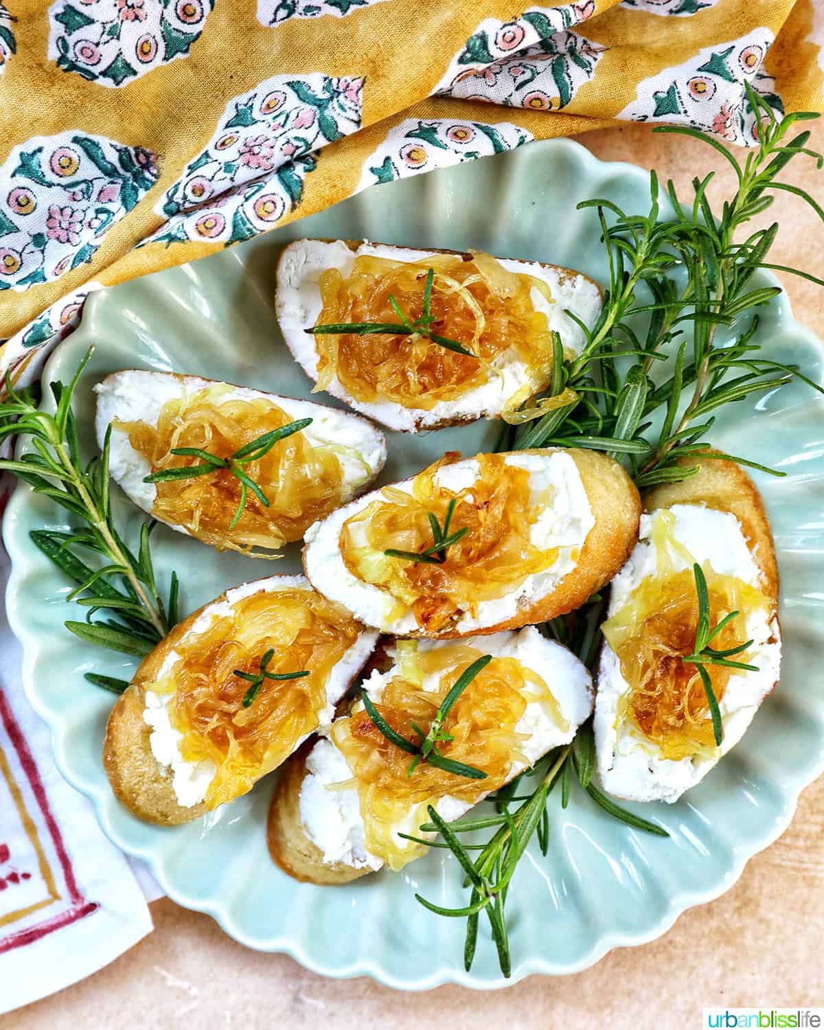 caramelized onions and goat cheese crostini on a plate with rosemary sprig garnish.