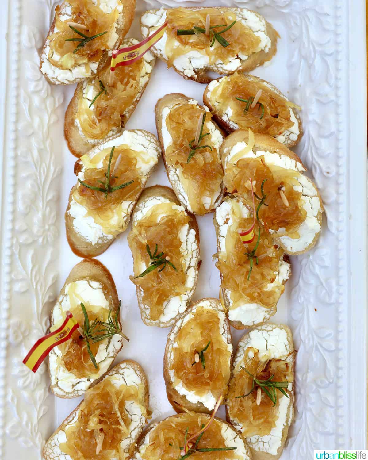 caramelized onions and goat cheese crostini on a plate with rosemary sprig garnish.