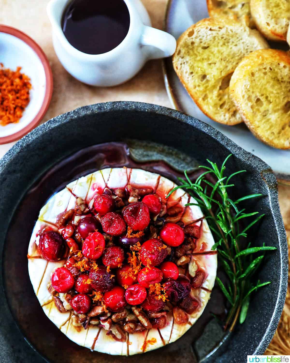 cranberry pecan baked brie in a skillet with side of crostini bread, honey.