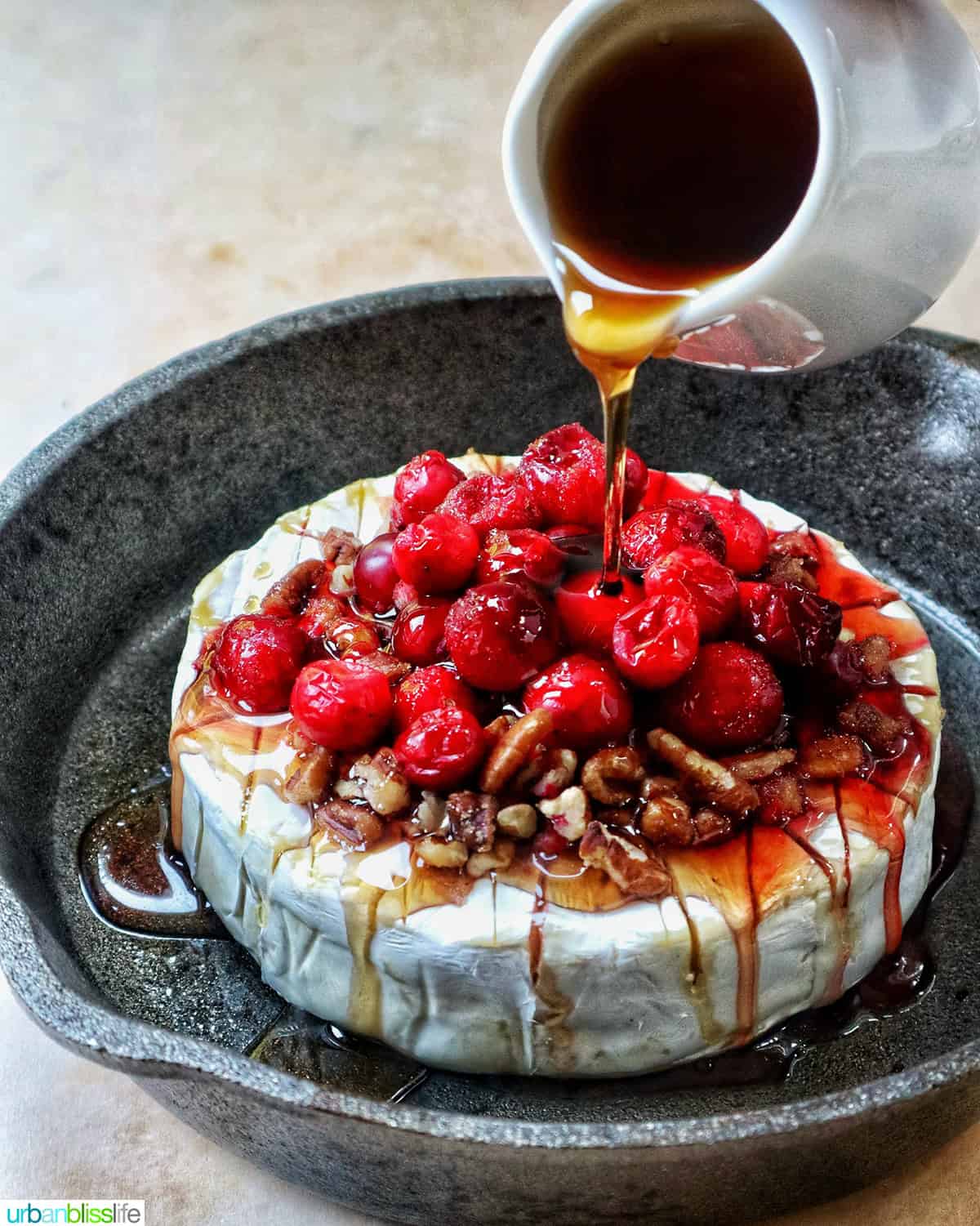 cranberry pecan baked brie in a skillet with honey pouring over the top.