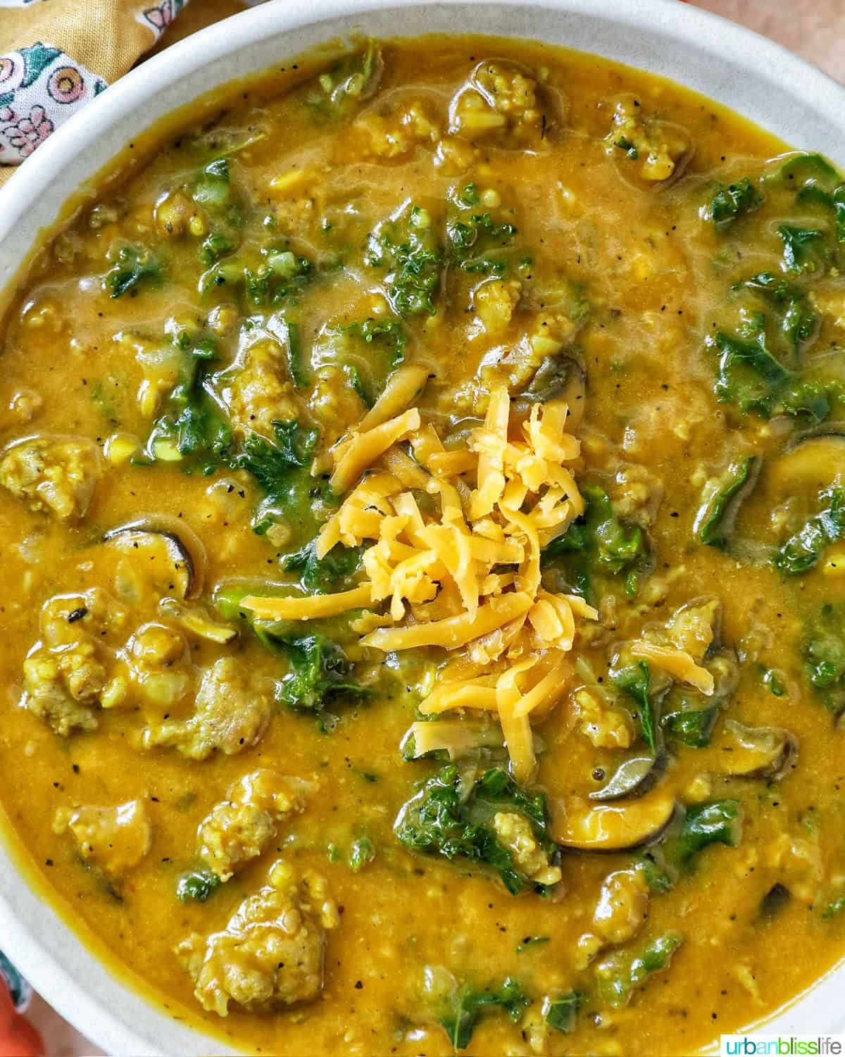 bowl of pumpkin soup with sausage, greens and cheese.