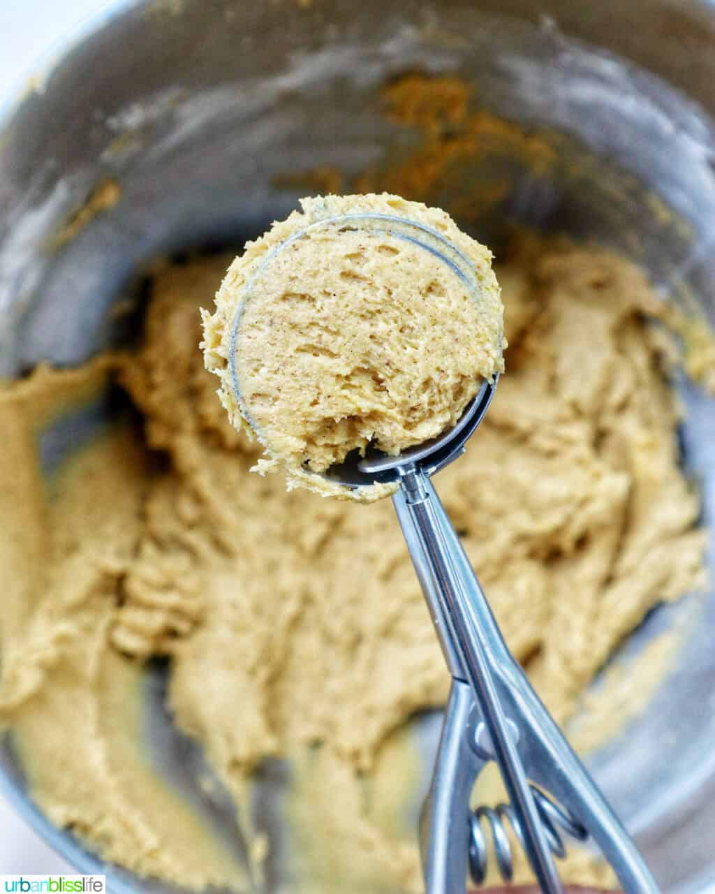 cookie scoop with pumpkin pie spice cookie batter in it above a bowl of batter.
