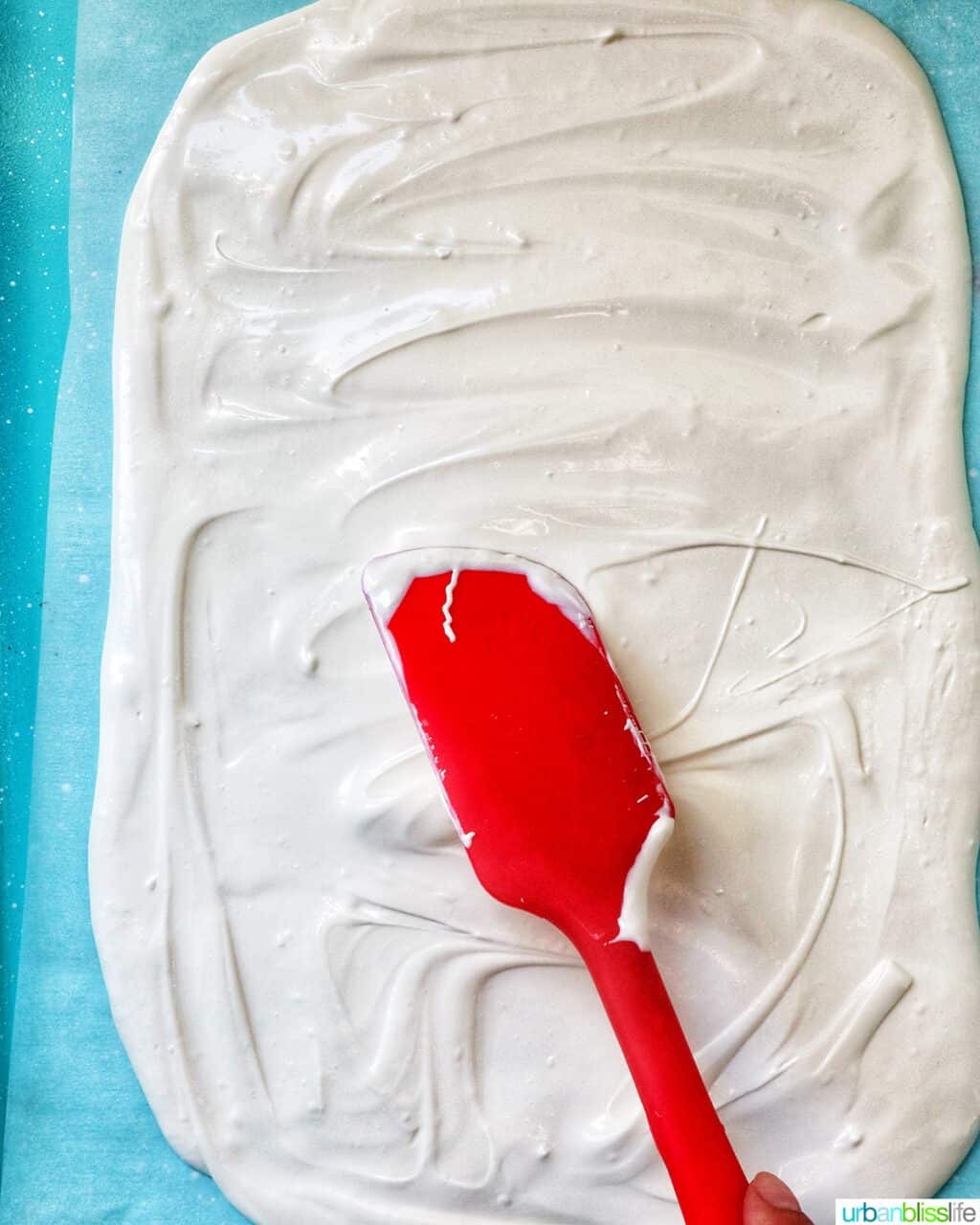 red spatula spreading melted white chocolate onto a baking sheet.