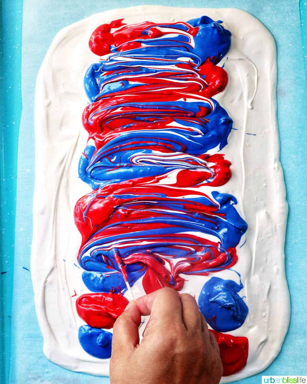 hand holding a toothpick, creating designs in the melted red, white, and blue chocolate bark.
