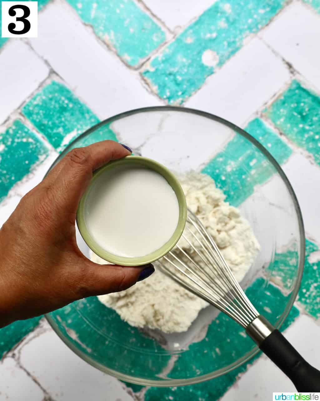 hand holding bowl of milk over batter.