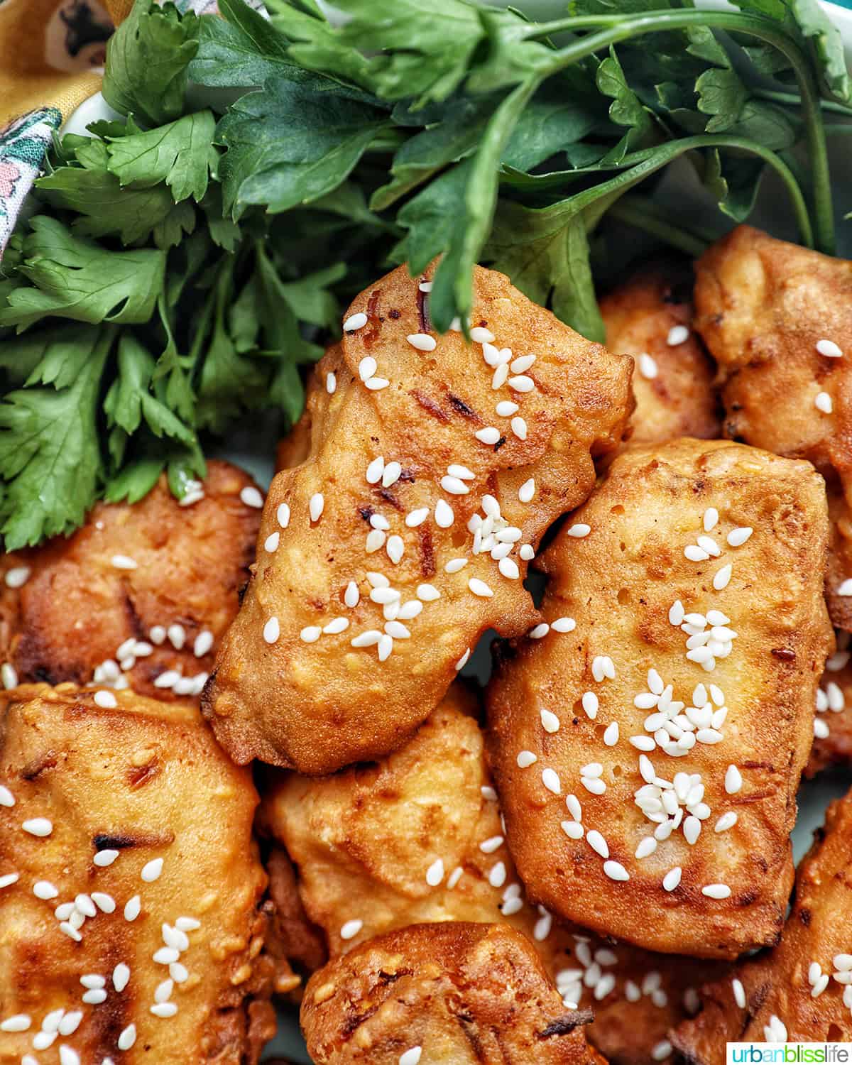 bowl of Thai fried bananas dessert with bowl of sesame seeds and herbs.