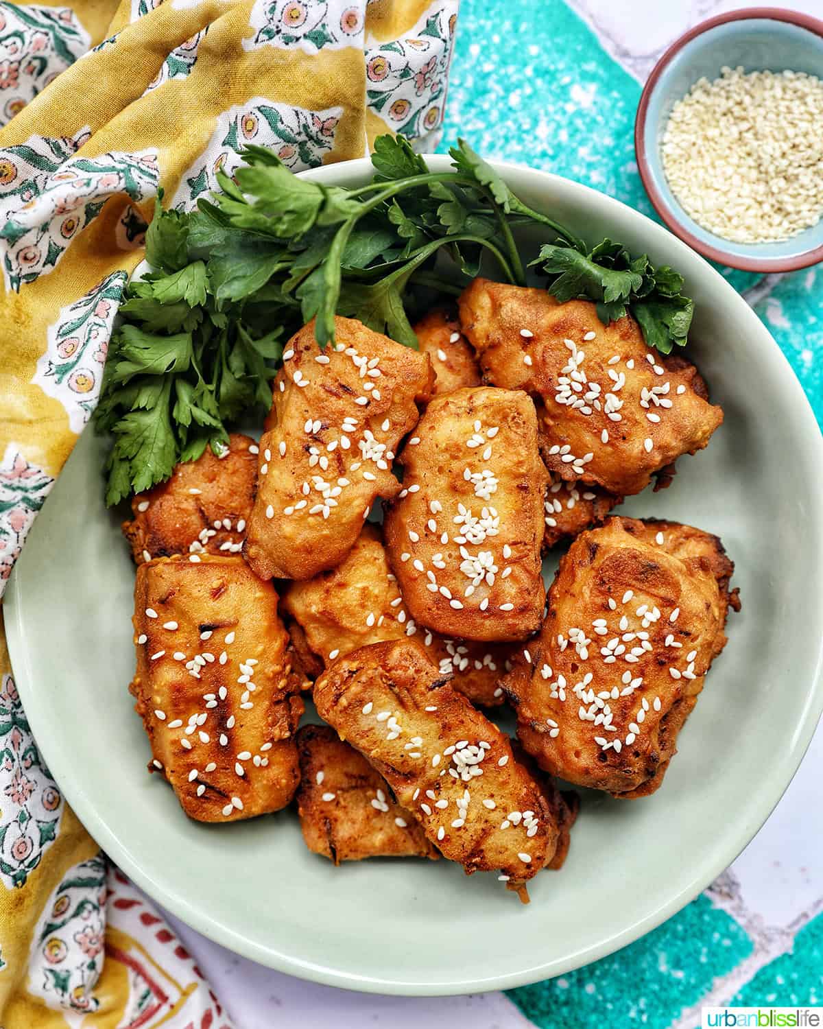 bowl of Thai fried bananas dessert with bowl of sesame seeds and herbs.
