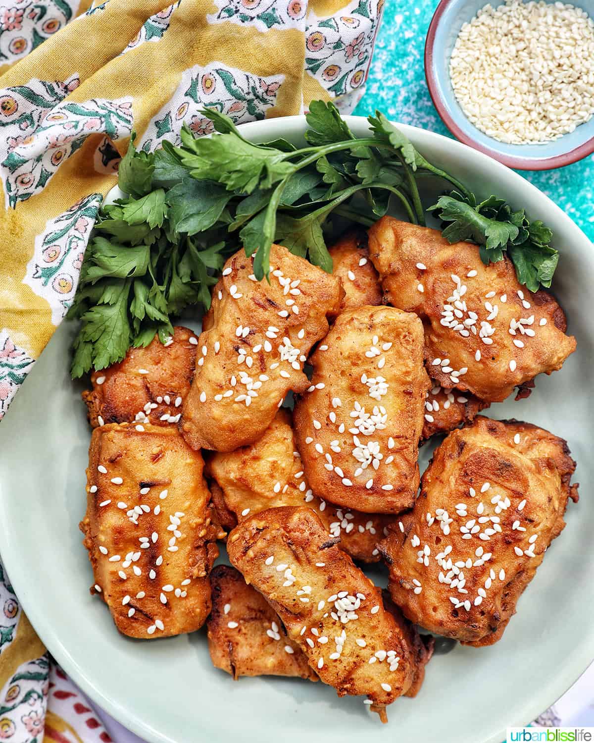 bowl of Thai fried bananas dessert with bowl of sesame seeds and herbs.