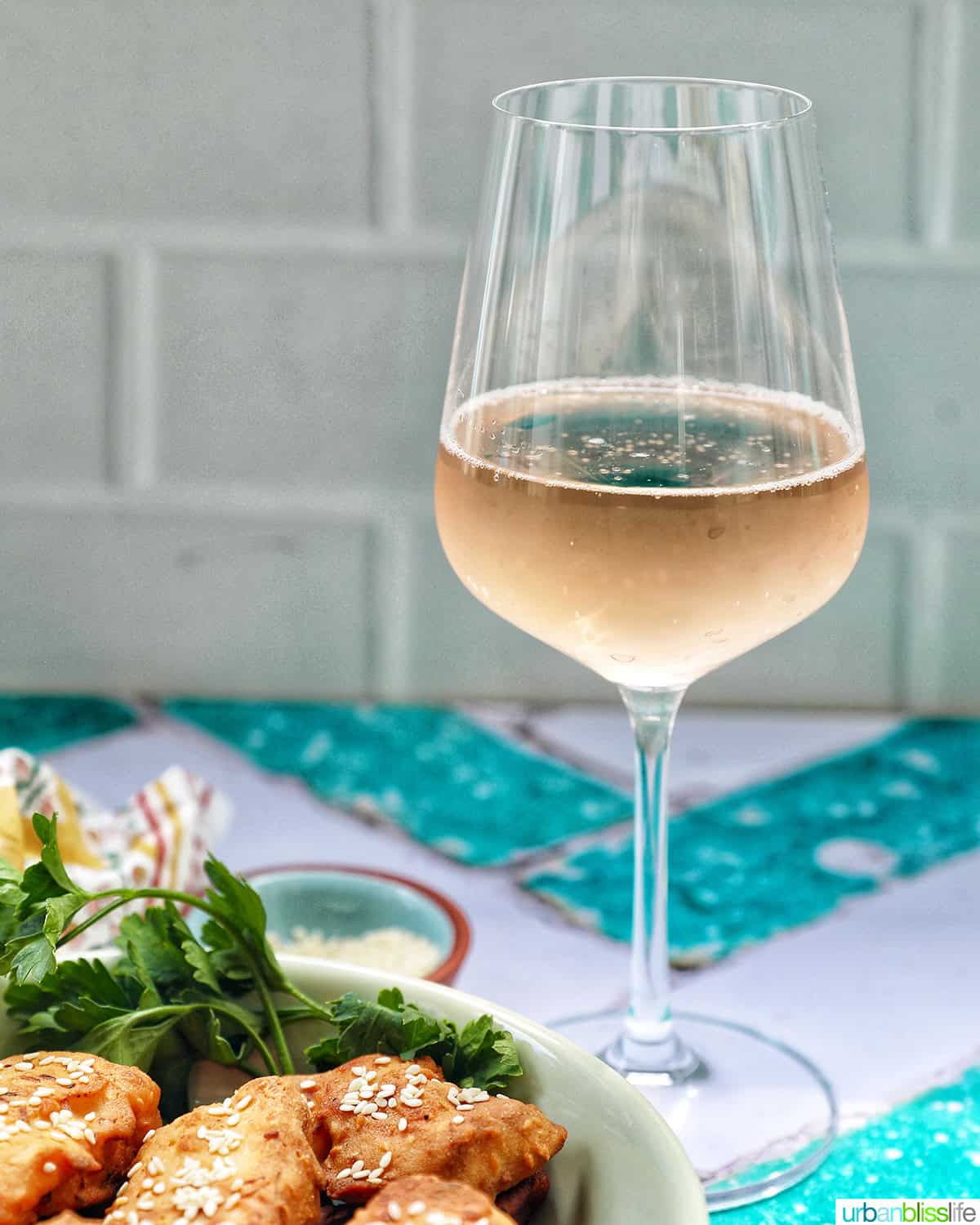 bowl of Thai fried bananas dessert with bowl of sesame seeds and herbs and glass of sparkling brut rose wine.
