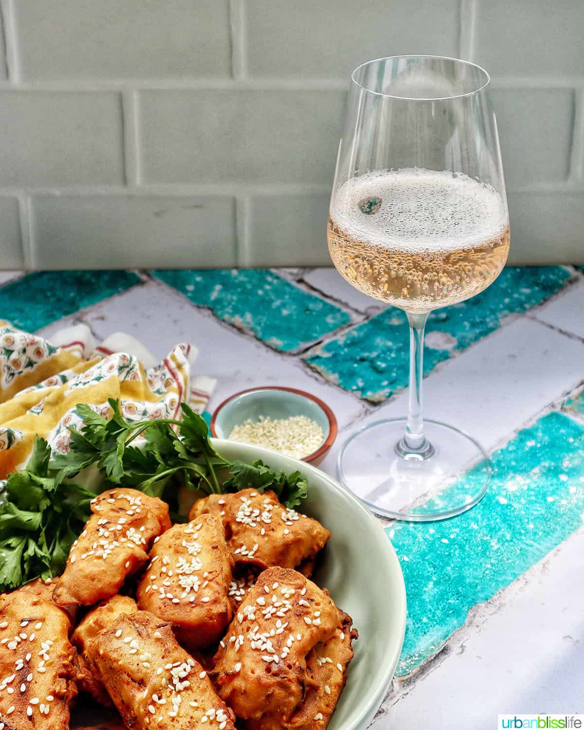 bowl of Thai fried bananas dessert with bowl of sesame seeds and herbs and glass of sparkling brut rose wine.