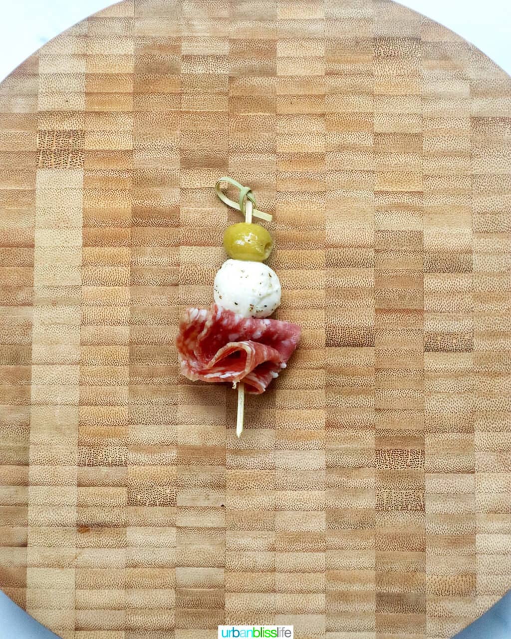 food pick with an olive, mozzarella ball, and salami on a cutting board.