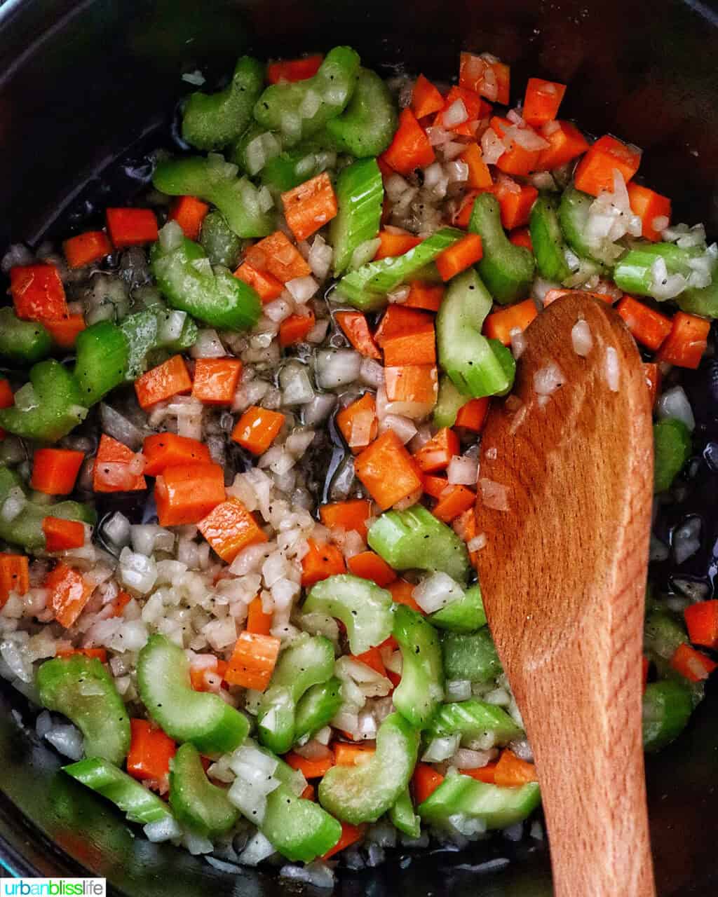 wooden spoon stirring mirepoix of carrots, celery, and onions in a Dutch oven.