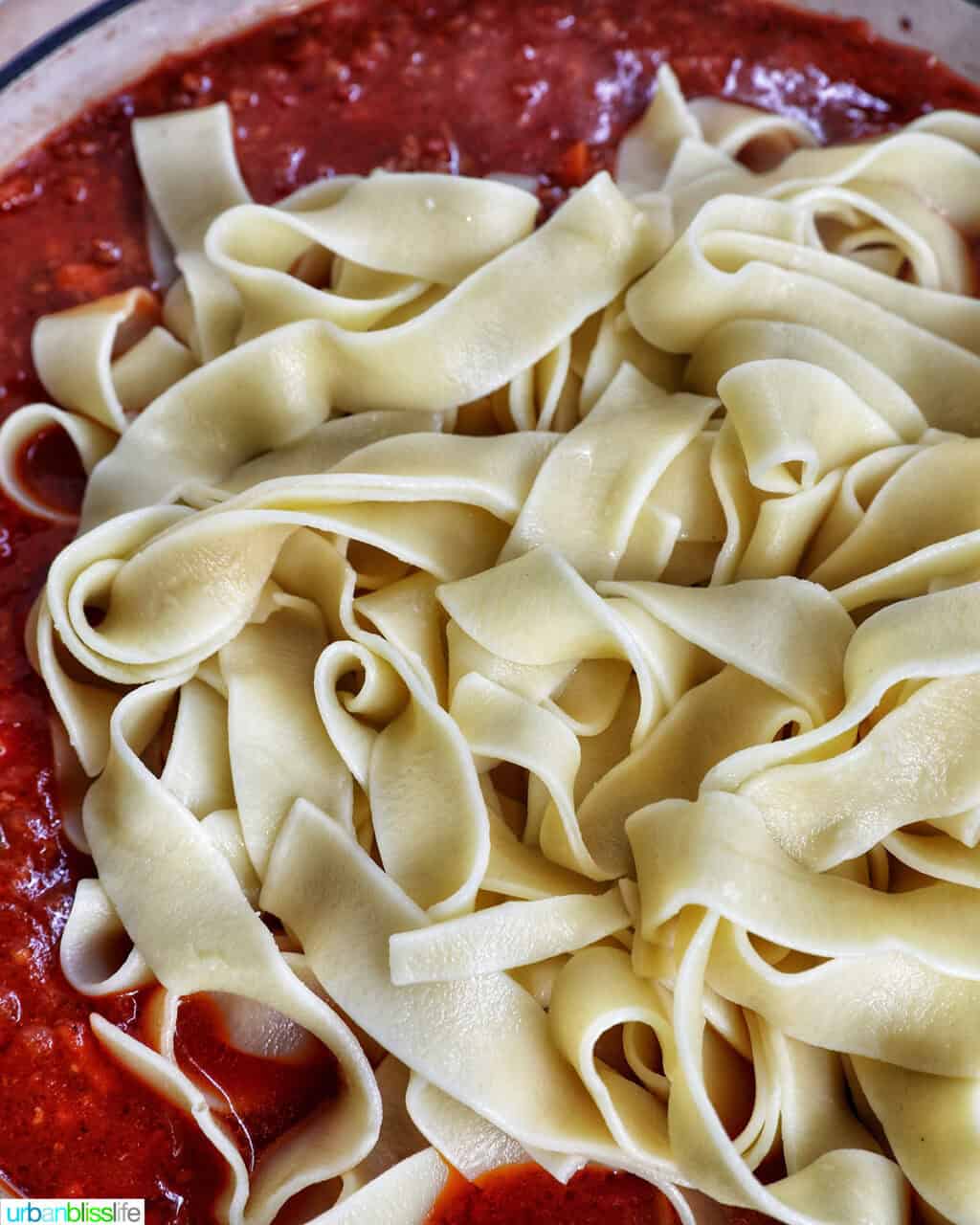 noodles added to a pan of lamb ragu pappardelle.
