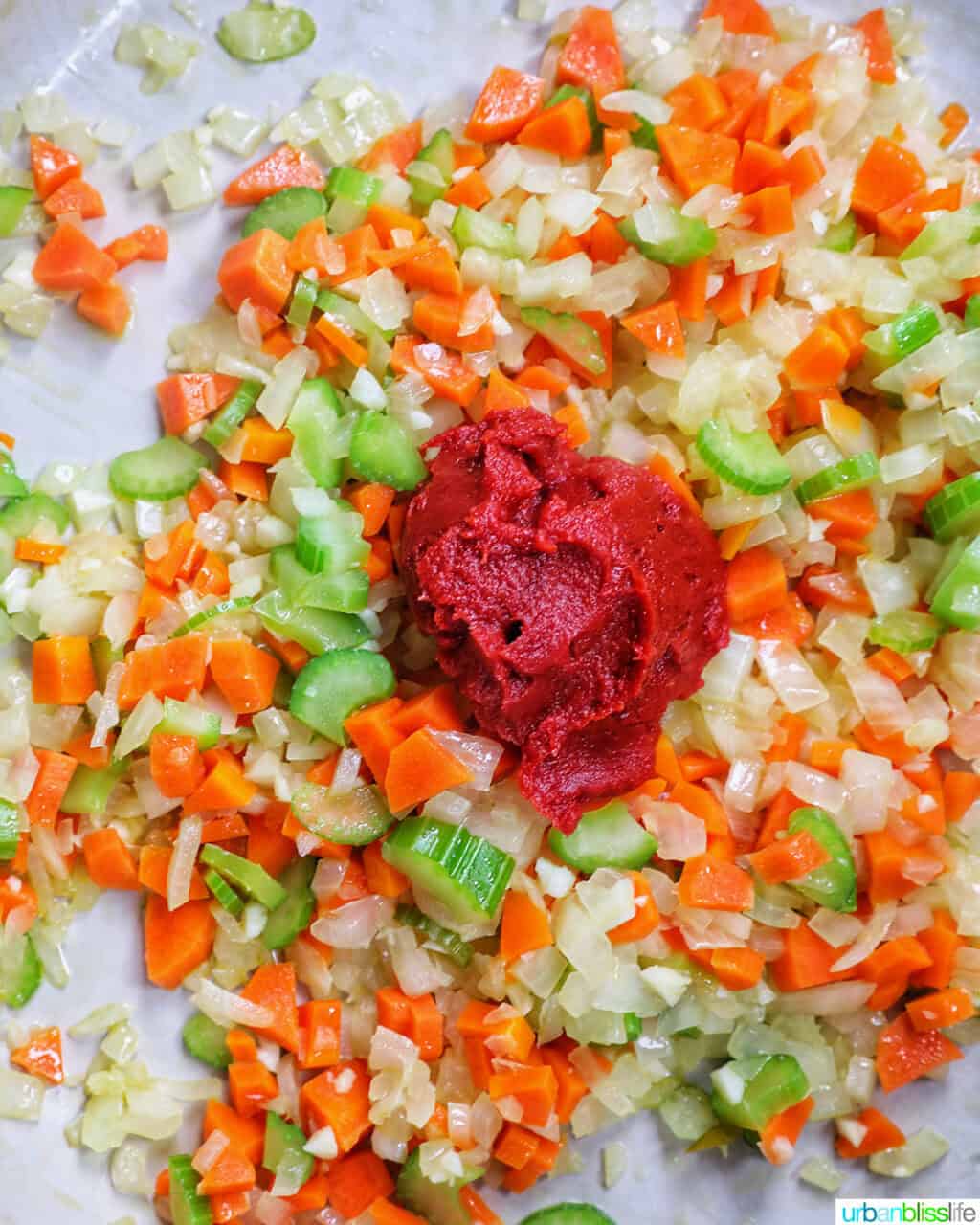 tomato paste added to carrots, onions, and celery in a pan.
