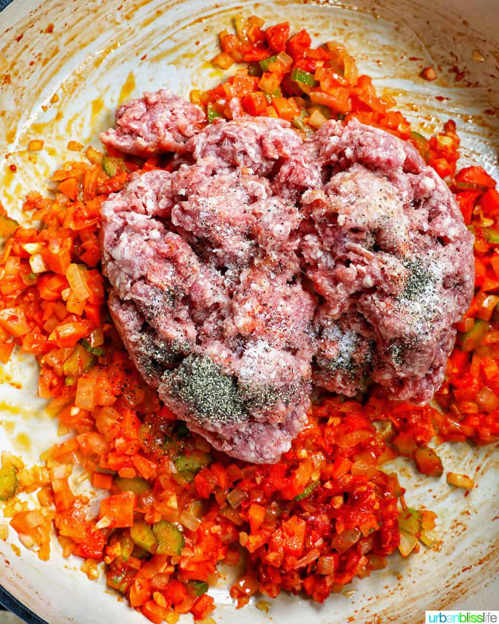 ground lamb added to a pan of carrots, onions, and celery in a pan.