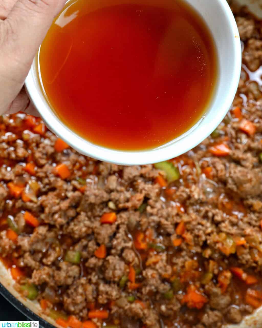adding beef broth to ground lamb, carrots, onions, and celery in a pan.
