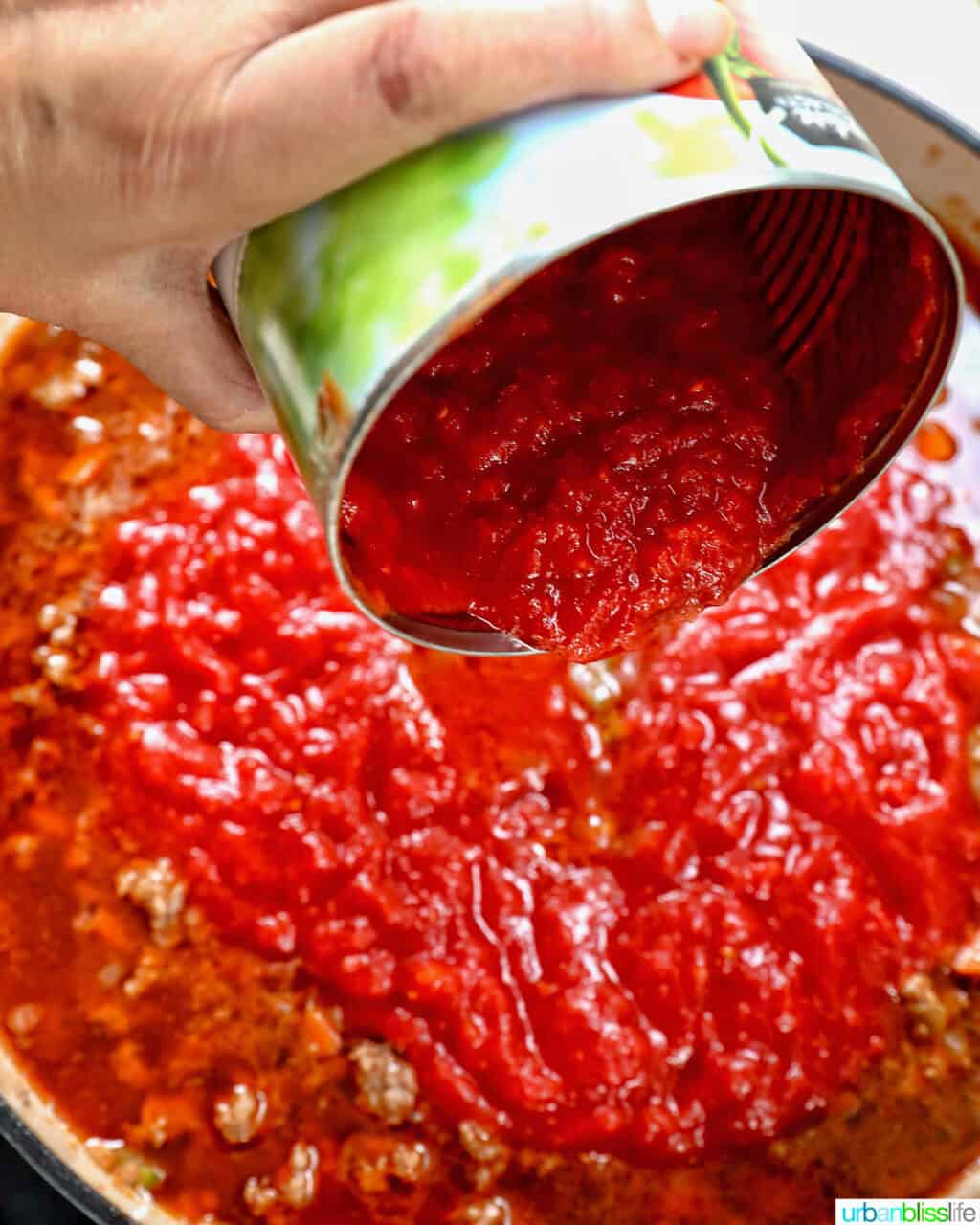 adding crushed tomatoes from a can to lamb ragu sauce.