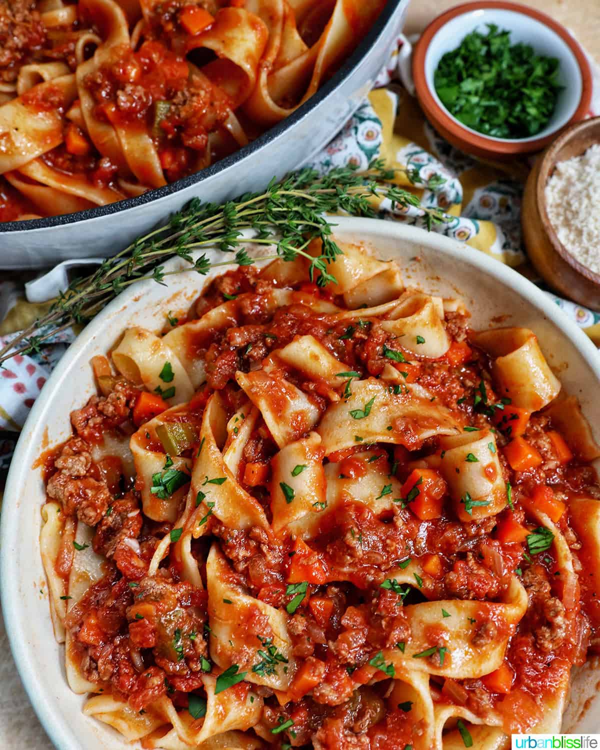 bowl of lamb ragu pappardelle with bowl of chopped parsley.