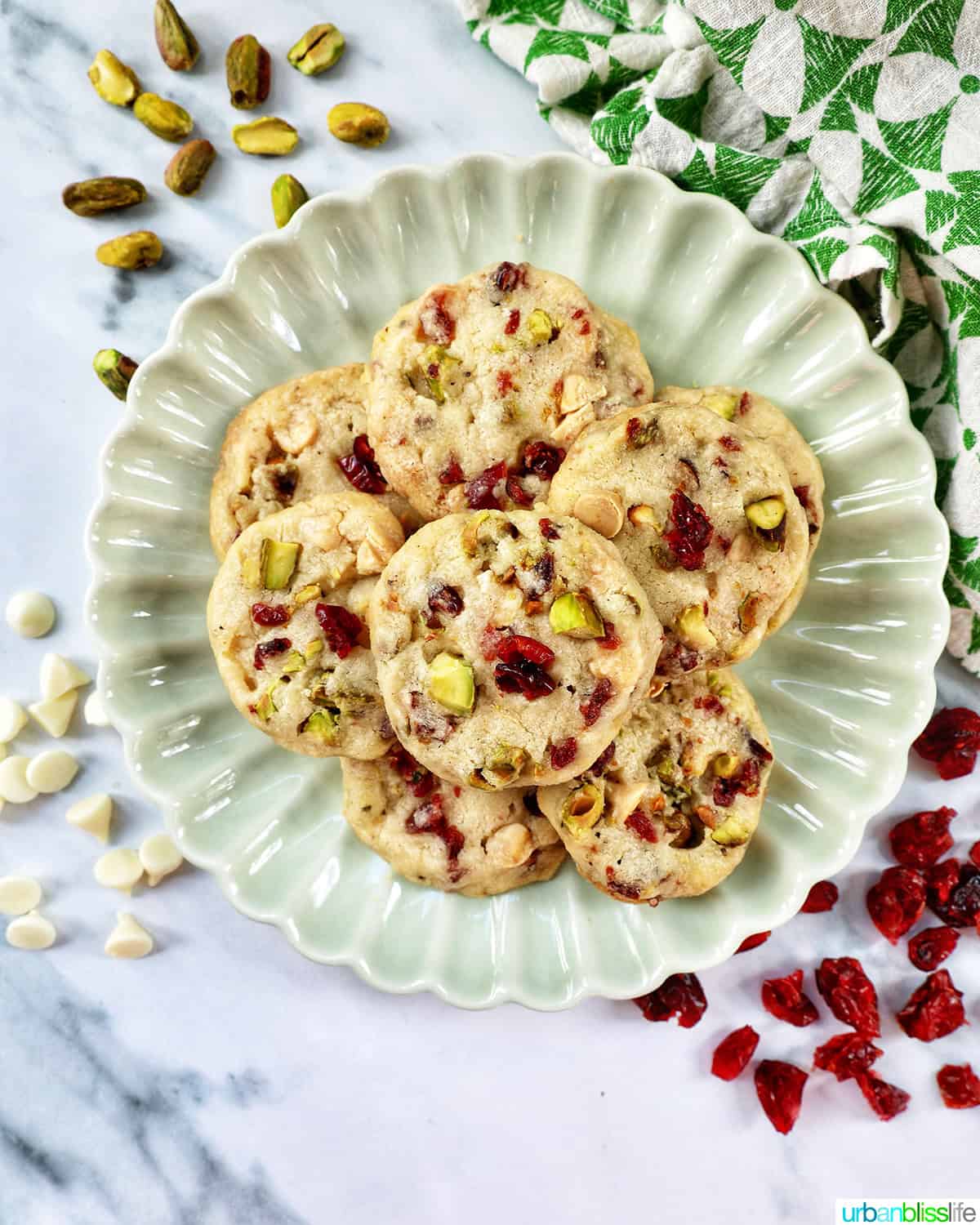plate of pistachio cranberry shortbread cookies surrounded by scattered ingredients.