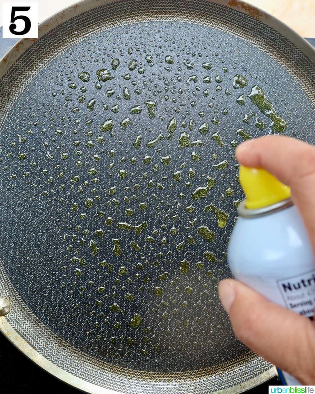 hand spraying cooking spray onto a griddle pan.