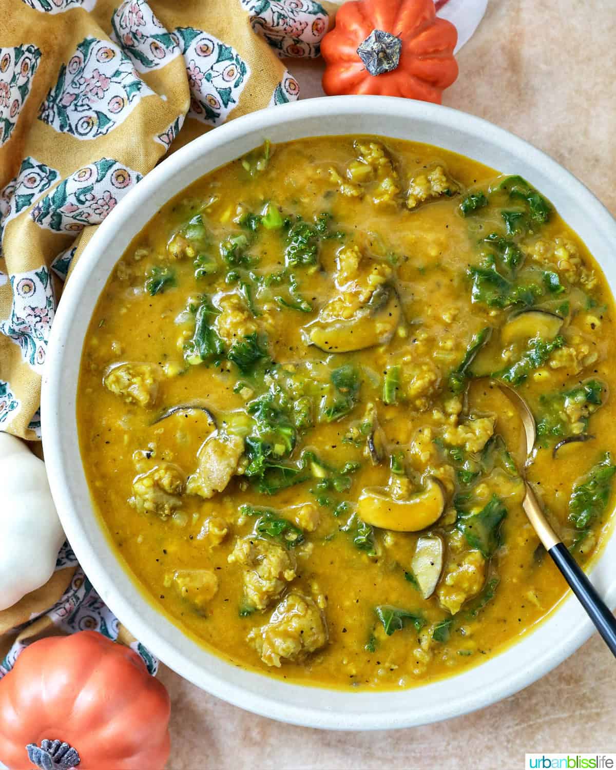bowl of pumpkin soup with sausage with spoon and side of small pumpkin decorations.