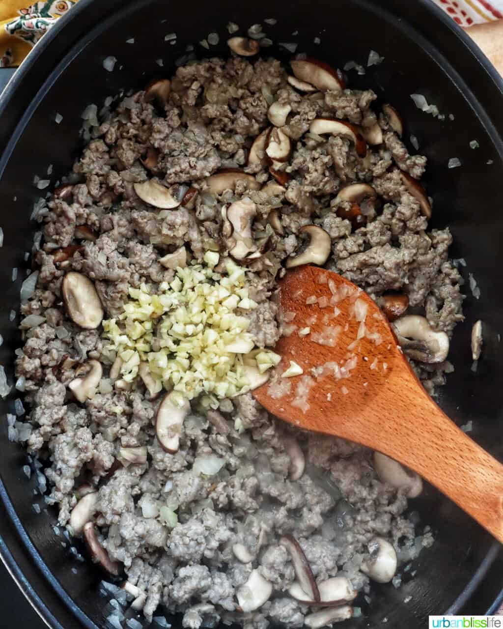 wooden spoon mixing ginger with ground meat and mushrooms in a dutch oven.