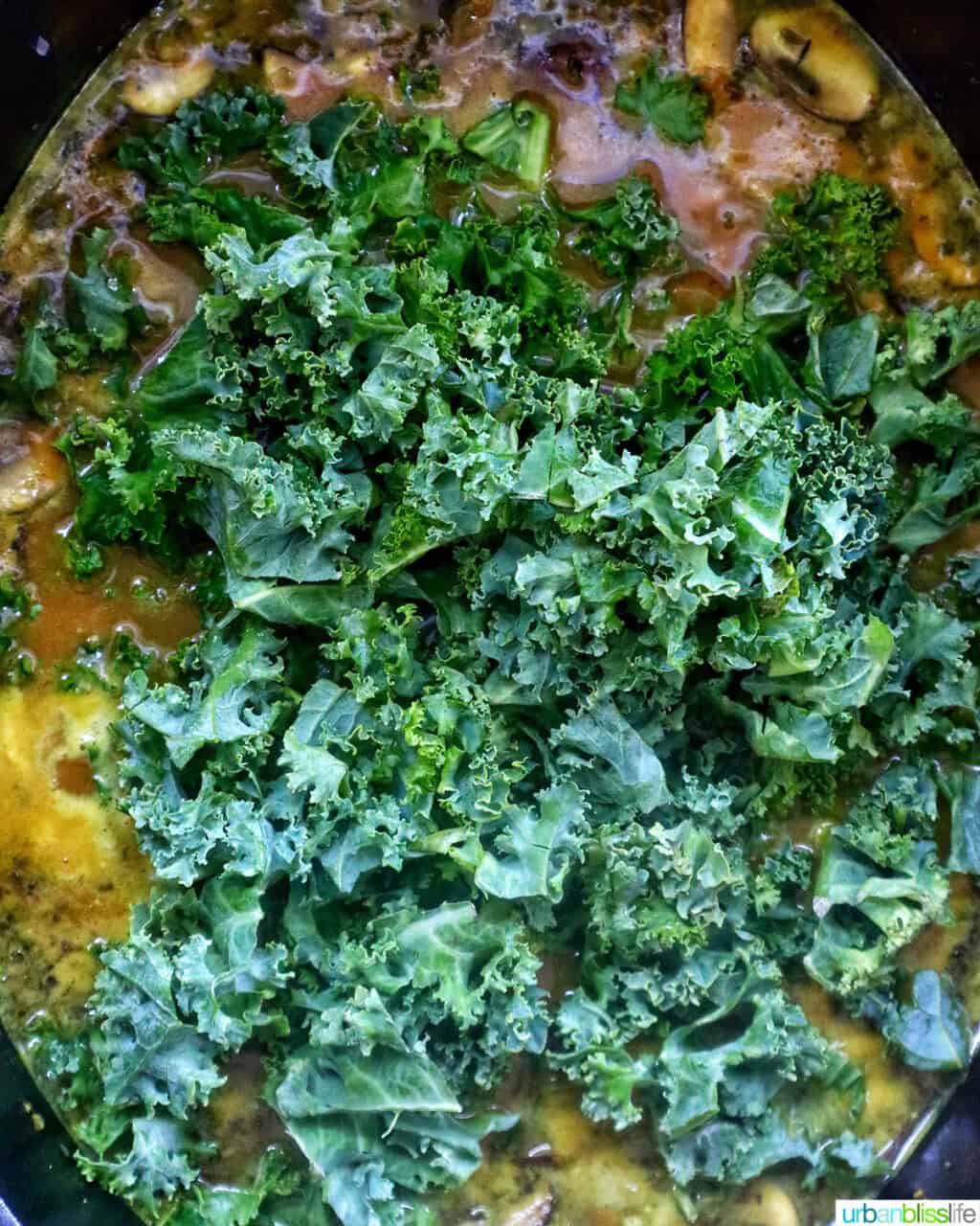 kale added to pumpkin sausage soup in a pot.