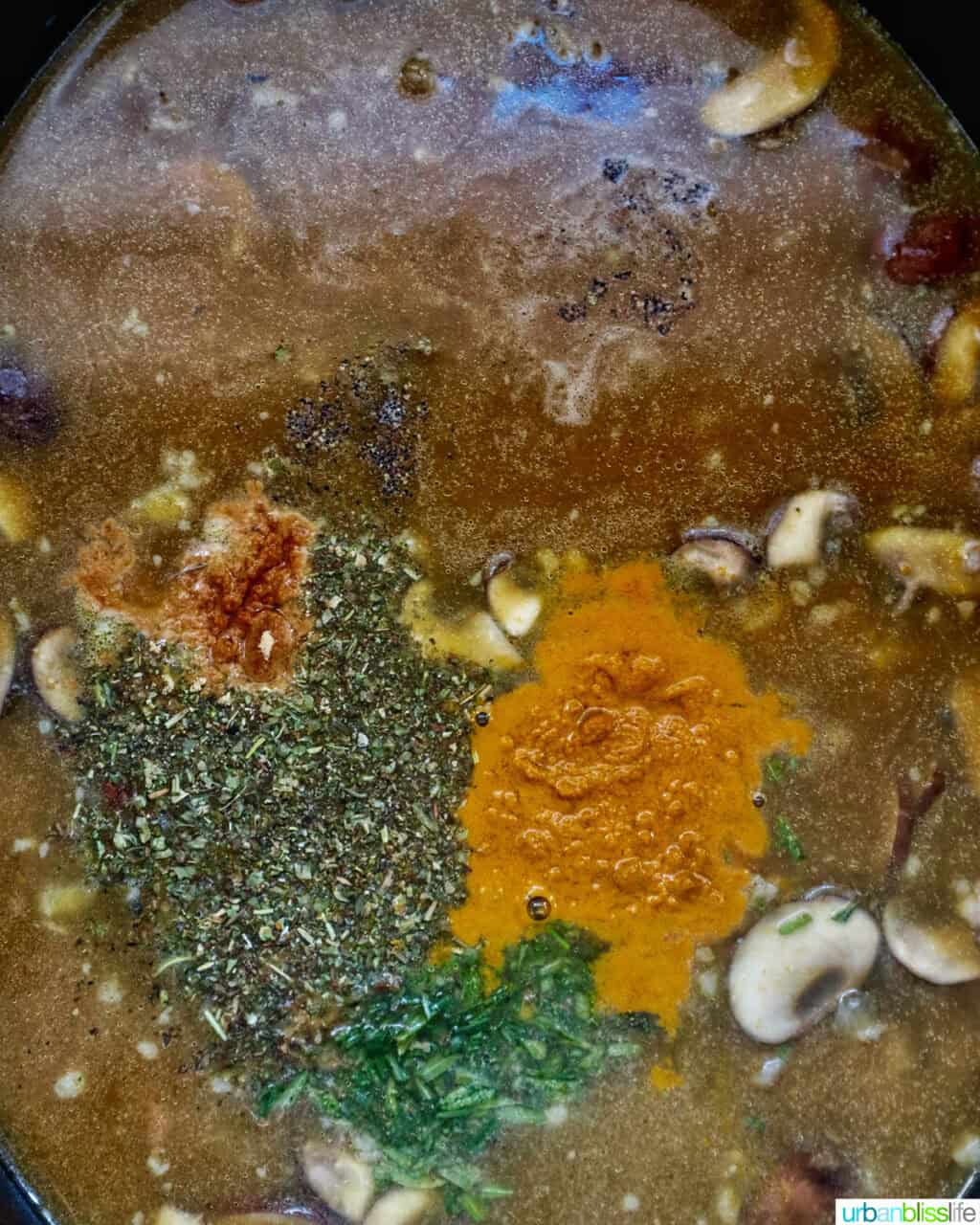spices and herbs added to pumpkin sausage soup in a dutch oven.