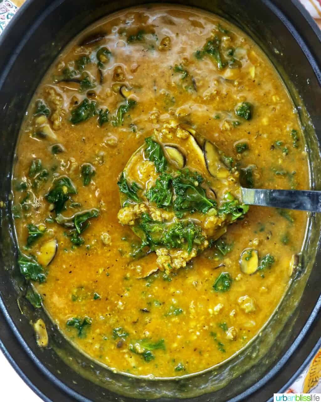 ladle full of pumpkin soup with sausage in a dutch oven.