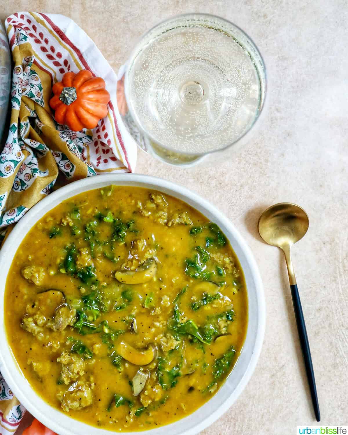 bowl of pumpkin soup with sausage next to a spoon and glass of white wine.