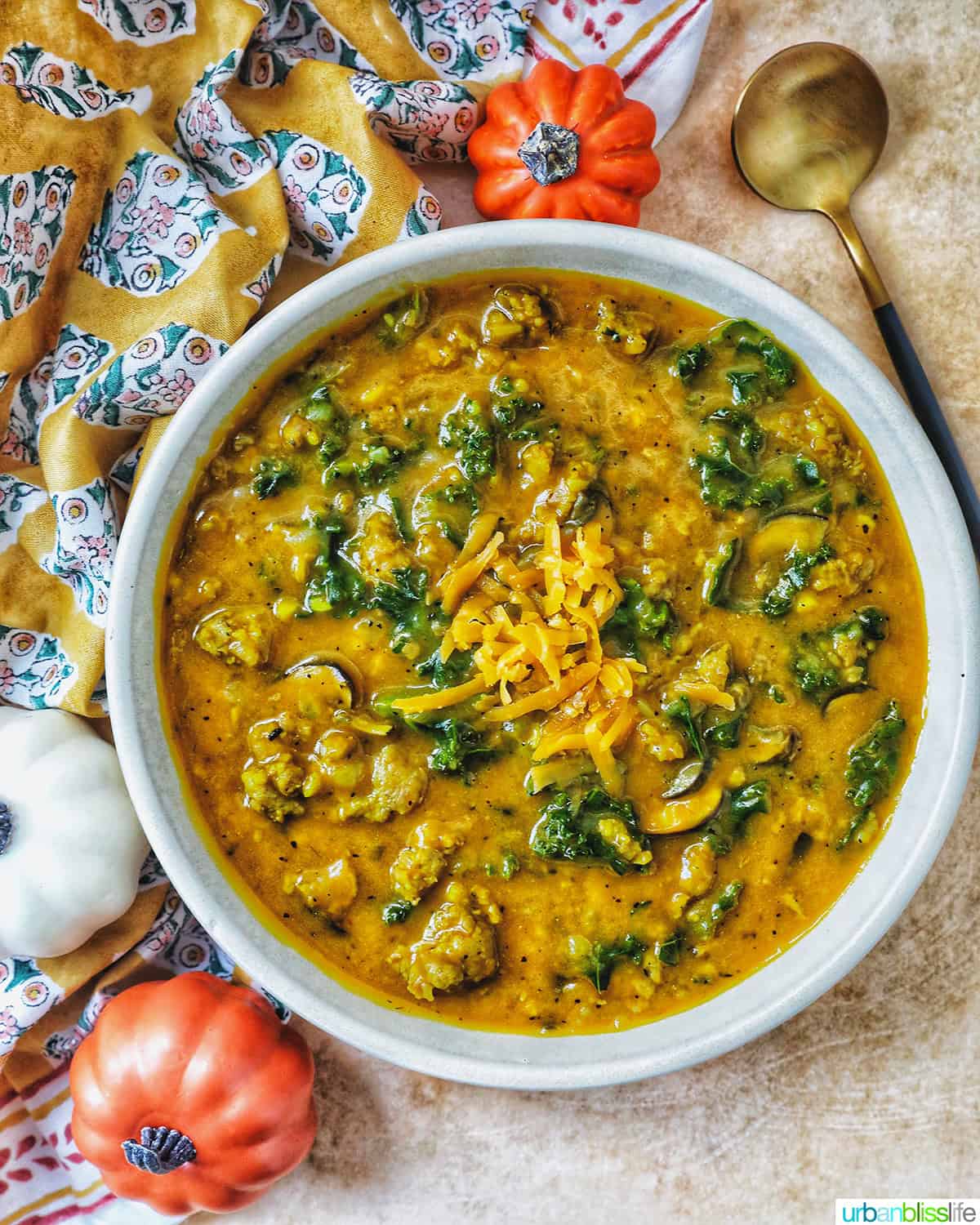bowl of pumpkin soup with sausage with spoon and side of small pumpkin decorations.