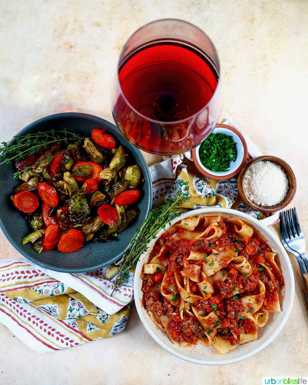 roasted brussels sprouts and carrot slices in a bowl with a glass of red wine and bowl of lamb ragu pappardelle.