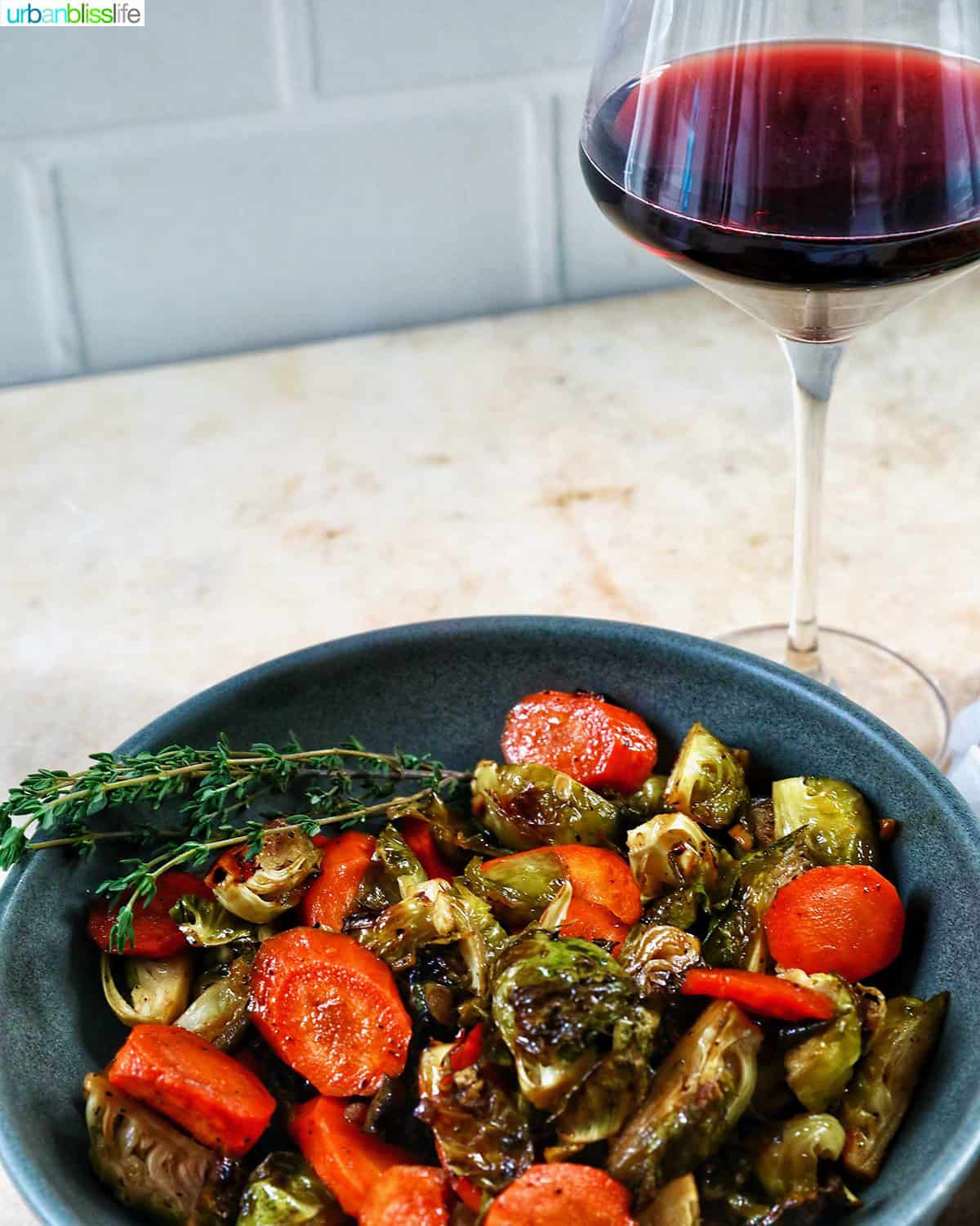 roasted brussels sprouts and carrot slices in a bowl with a glass of red wine.
