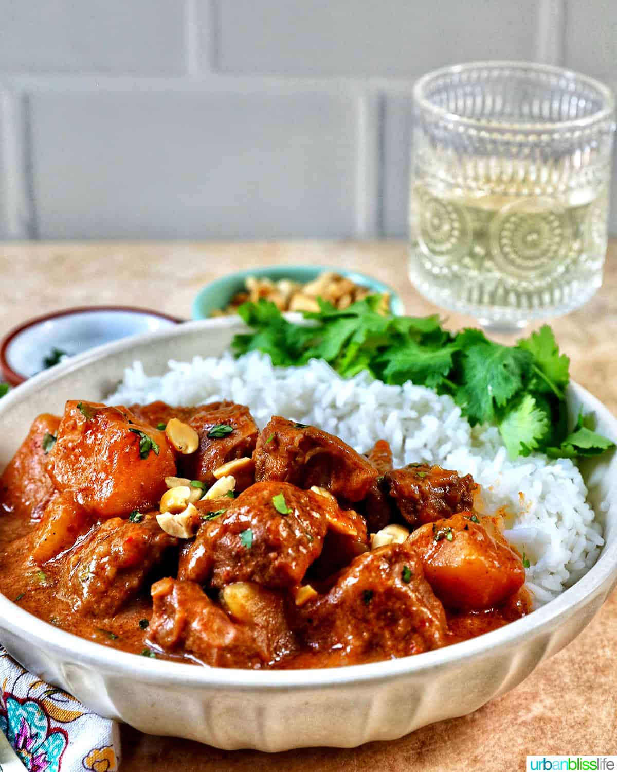 slow cooker beef massaman curry with rice in a bowl and glass of white wine.