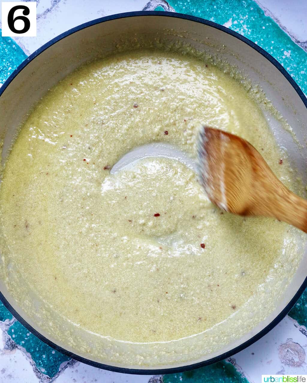 wooden spoon stirring tahini pasta sauce in a pan.