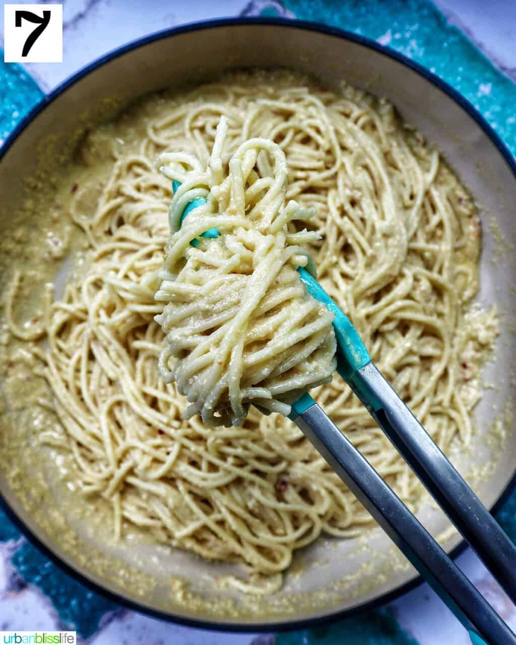 tongs holding up tahini pasta in a pan.